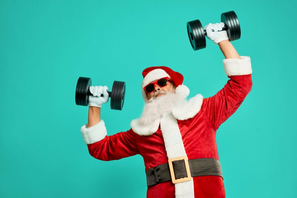 front view sportive santa claus holding dumbbels isolated crop funny senior man christmas costume sunglasses posing